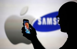 A man is silhouetted against a video screen with Apple and Samsung logos as he poses with a Samsung Galaxy S4 in this photo illustration taken in the central Bosnian town of Zenica
